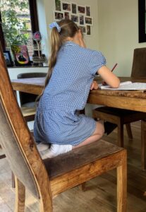 Child sitting on their knees on a dining chair